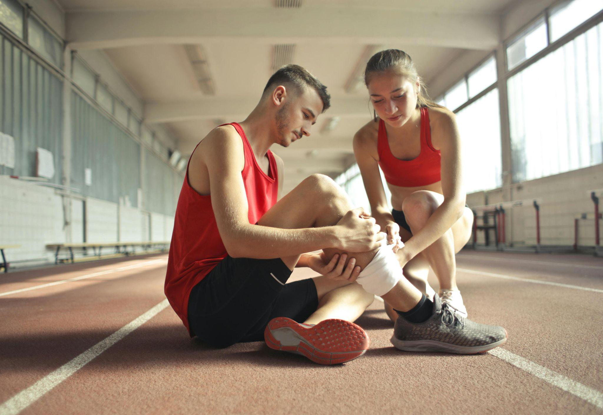 A girl wrapping a surgical bandage on an injured athlete’s leg