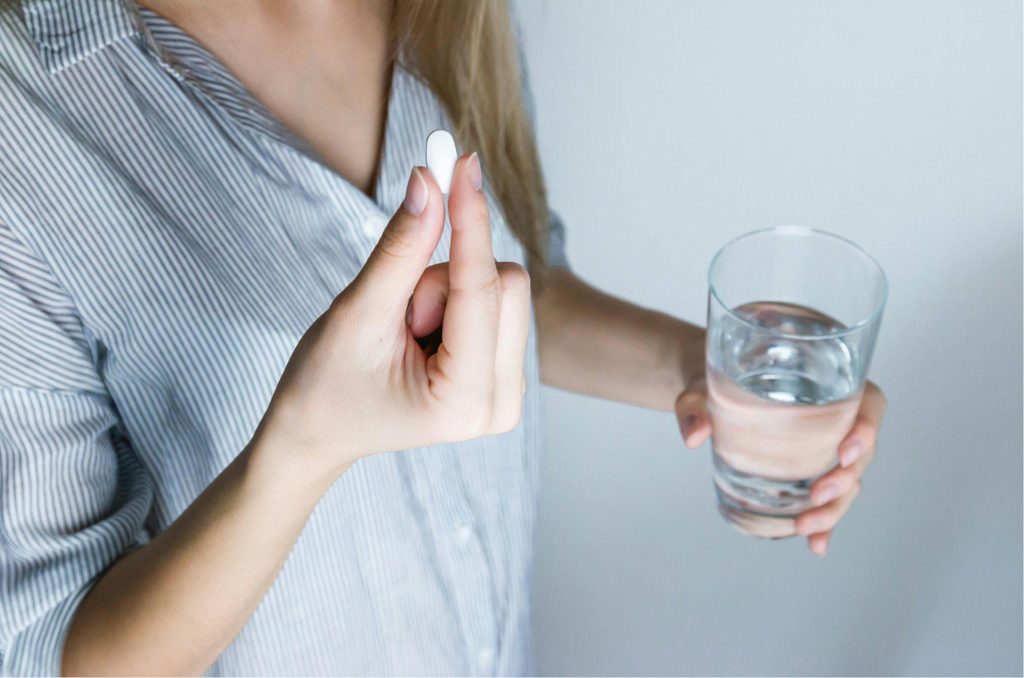 A woman holding a white pill and a glass half full of water.