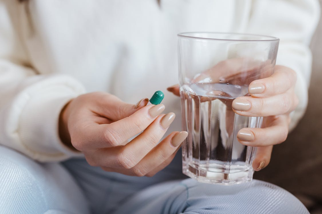 A woman holding a glass of water and a pill