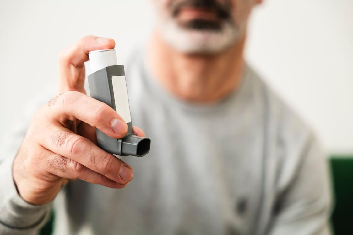 The image shows a person holding an inhaler, likely for asthma treatment.