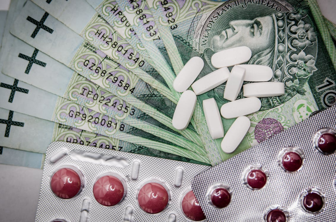 The image shows a stack of banknotes with pills, including white tablets and capsules, placed on top of them.