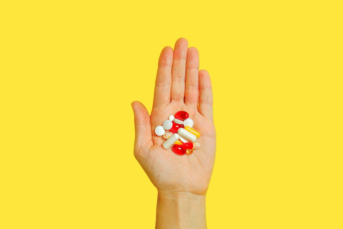 Closeup of a hand holding several medication pills, representing the process of managing prescriptions and seeking financial assistance.