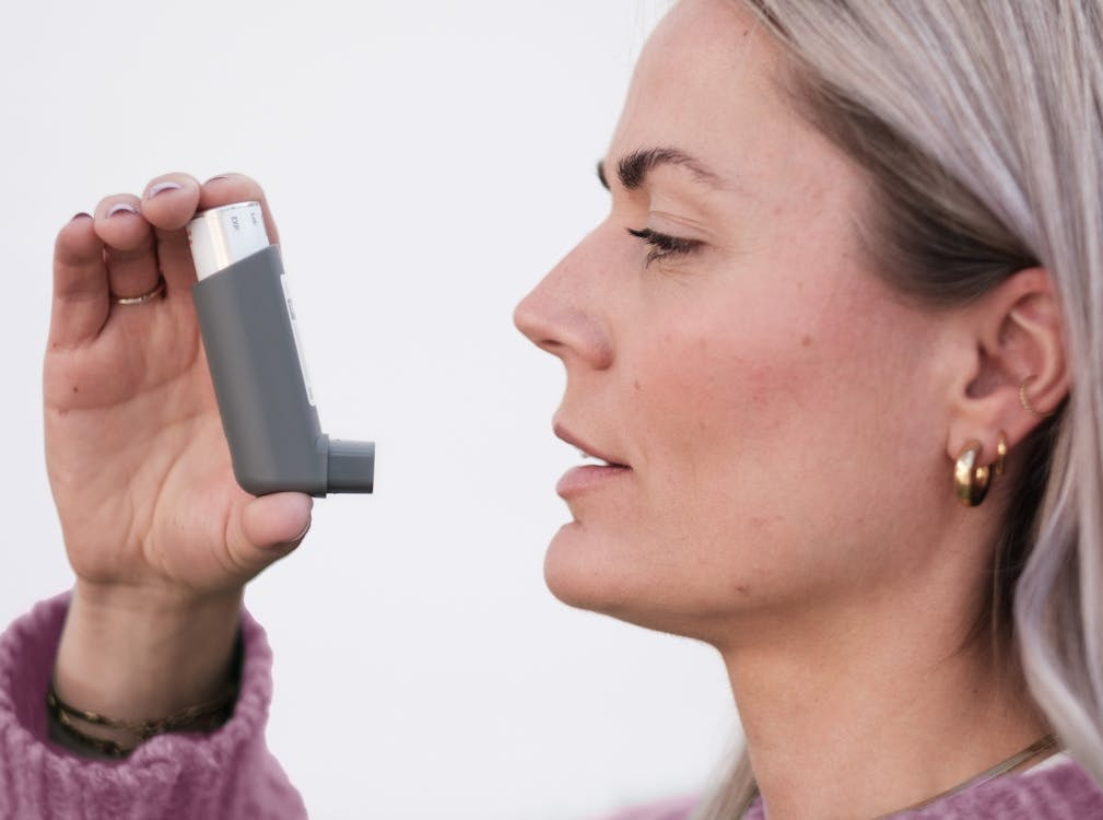 Woman using an inhaler against a clean white background, illustrating medication use for respiratory conditions.