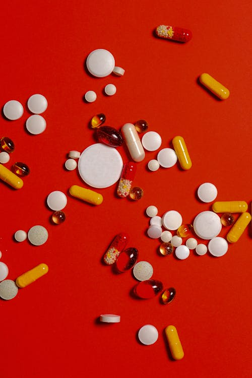 Assorted pills and capsules scattered on a red background