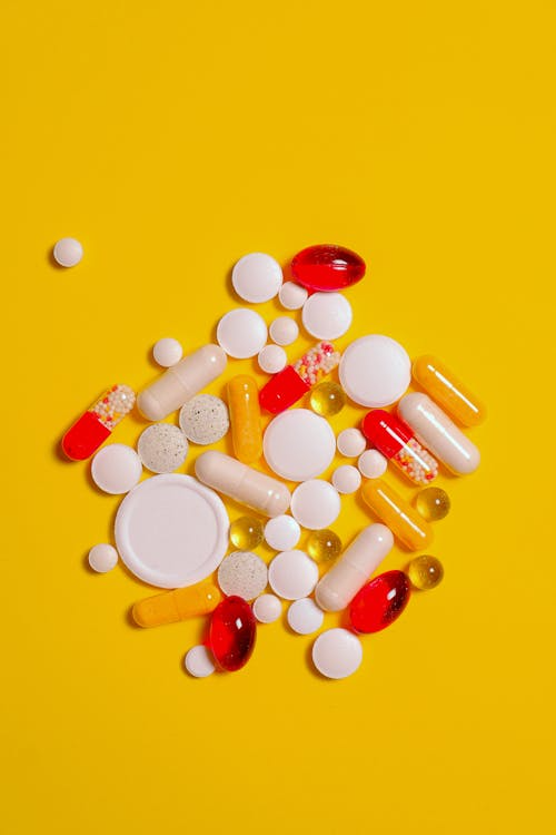 Assorted pills and capsules arranged on a bright yellow background