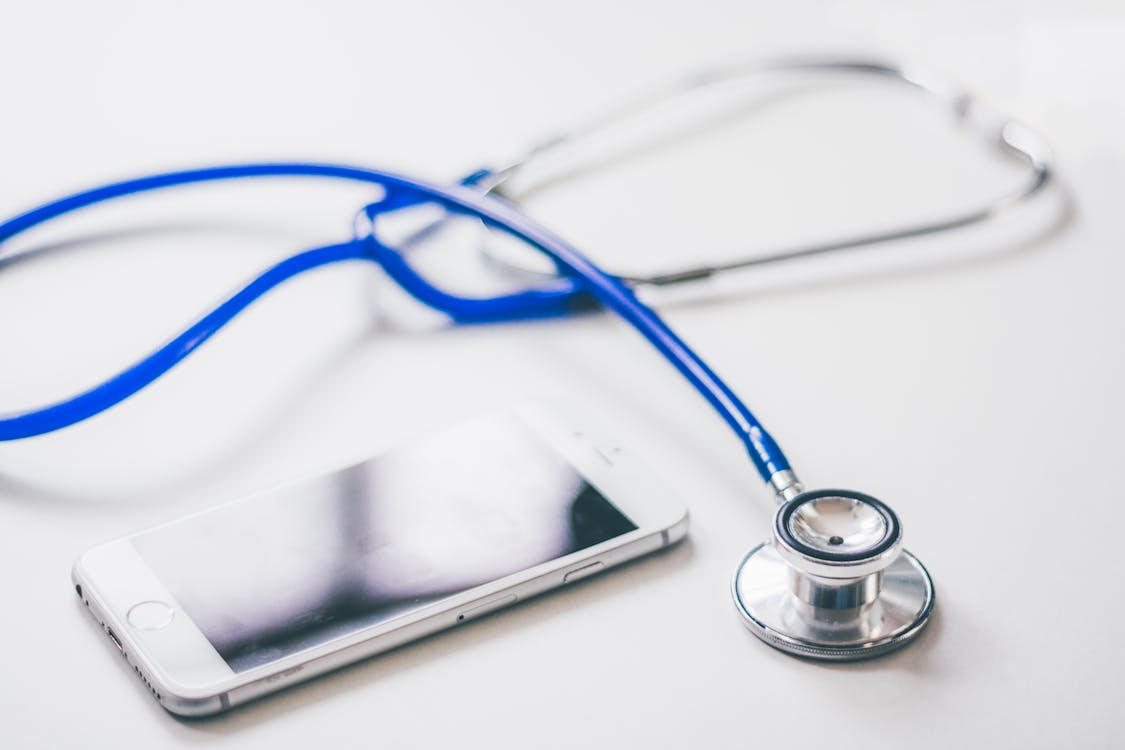 Blue stethoscope resting next to a smartphone on a white surface