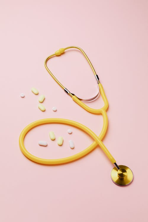 Yellow stethoscope with scattered pills on a pink background