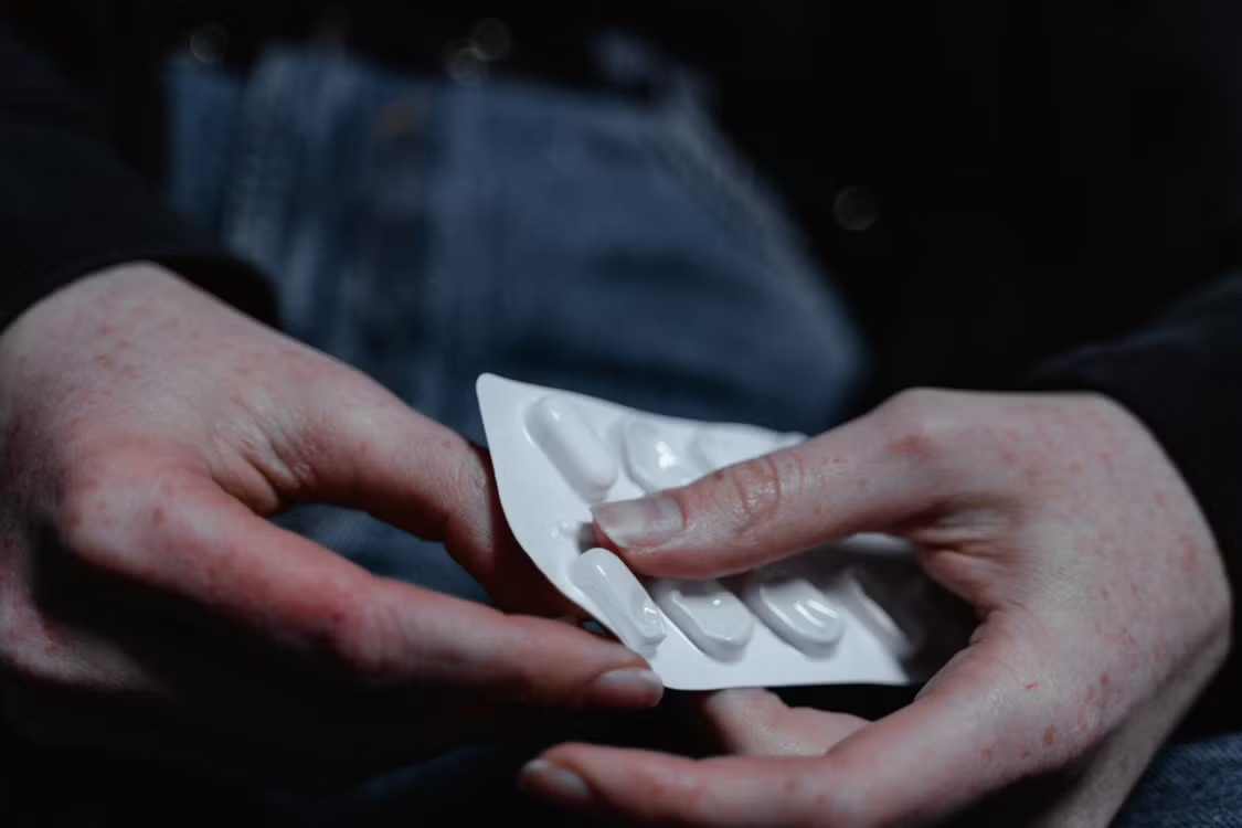 A person holding a blister pack of white prescription tablets in their hands.