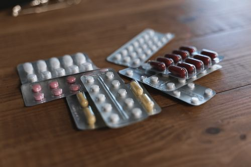 Several blister packs of mixed prescription medications on a wooden surface.
