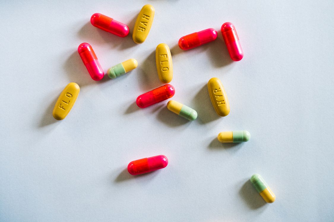 Scattered red, yellow, and green prescription capsules and tablets on a white surface.
