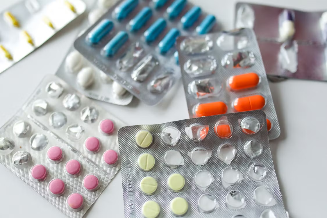 Multiple blister packs of pink, blue, orange, and yellow prescription medications scattered on a white surface.