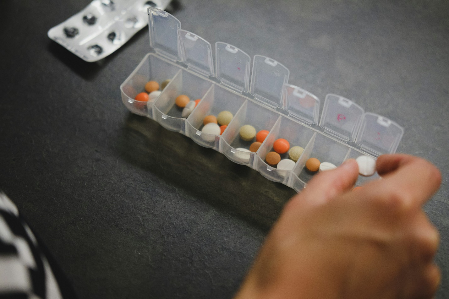 Person organizing daily medications in a pill organizer for proper medication management