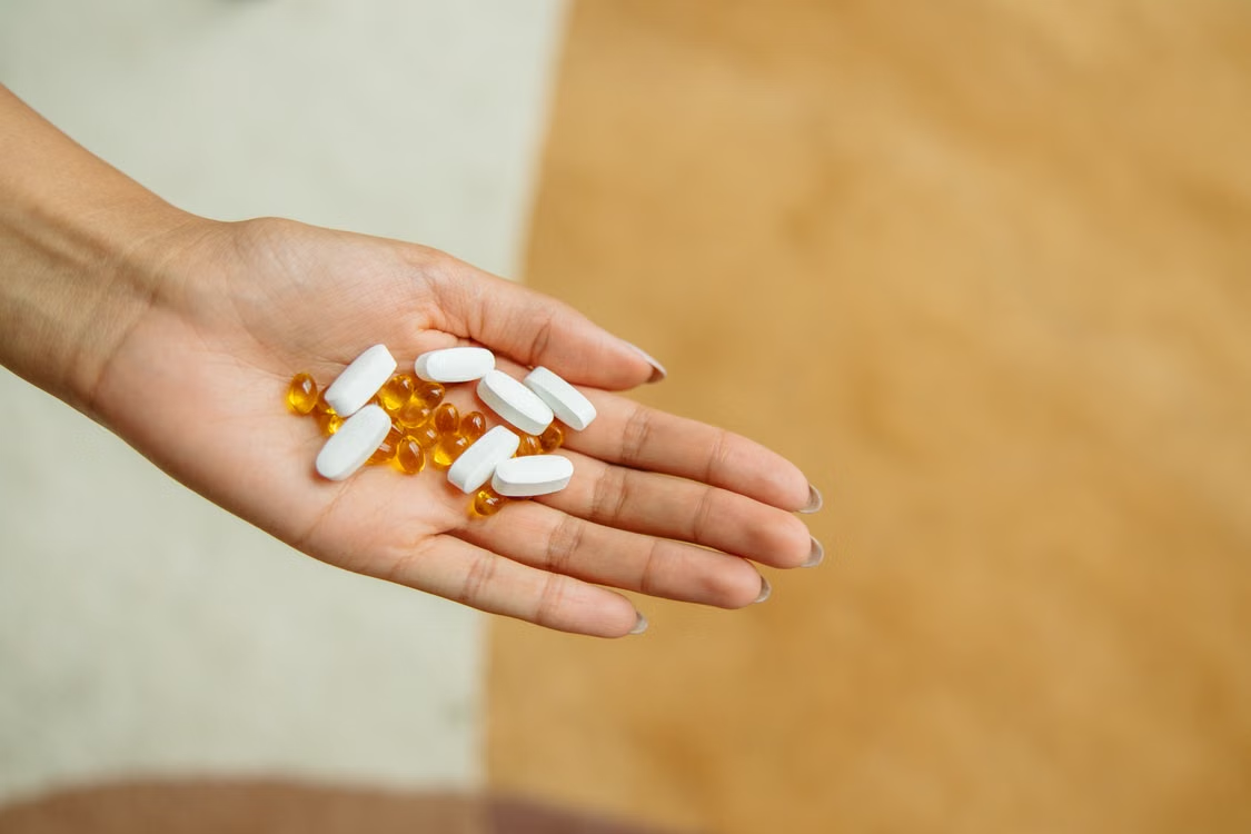 Patient holding prescribed tablets and softgel capsules in the palm of their hand