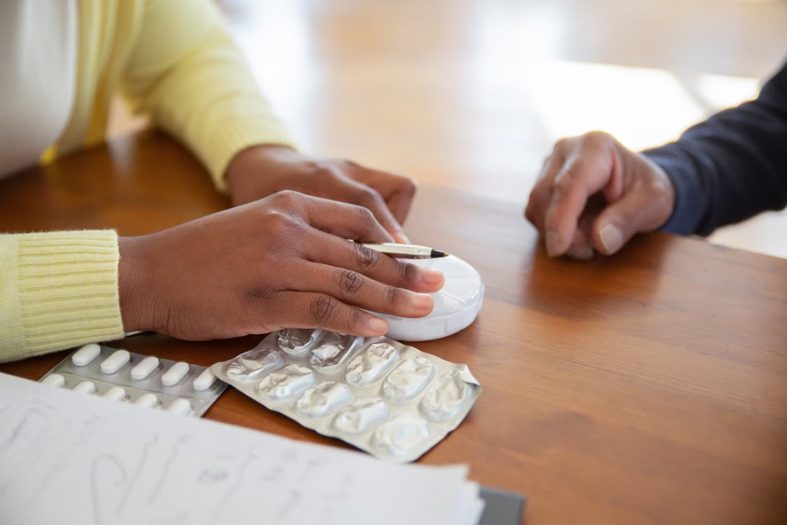 Caregiver organizing prescription medications with a pill organizer while assisting an older adult.