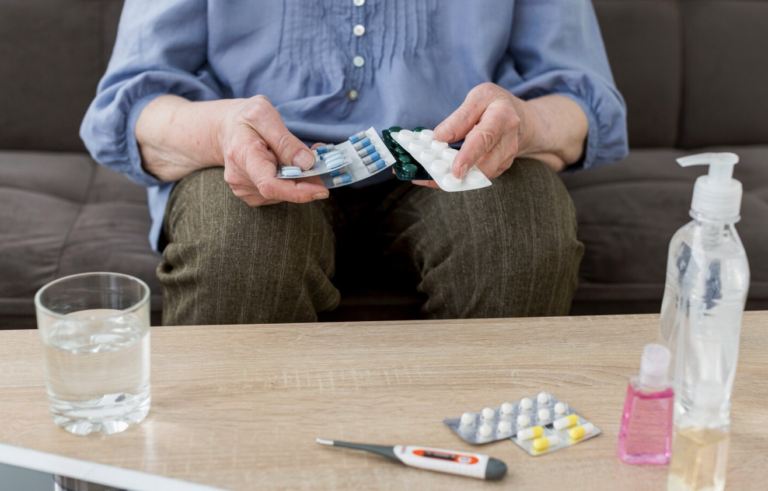 Older woman holding prescription medication while managing her ongoing healthcare needs.
