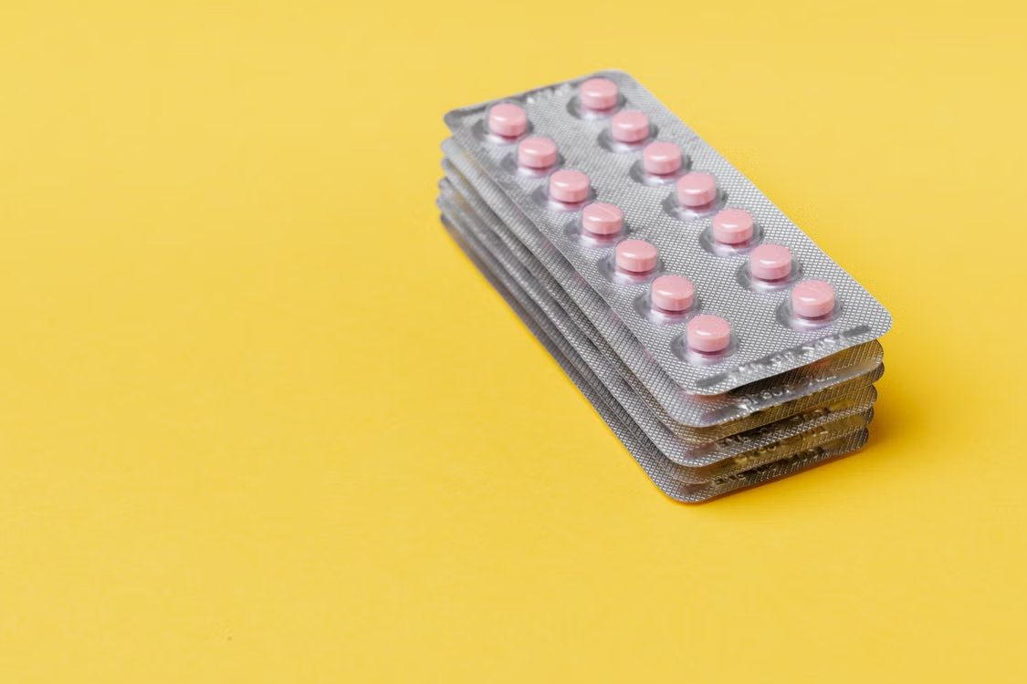 Stack of pink tablets sealed in individual blister packs on a bright yellow surface.