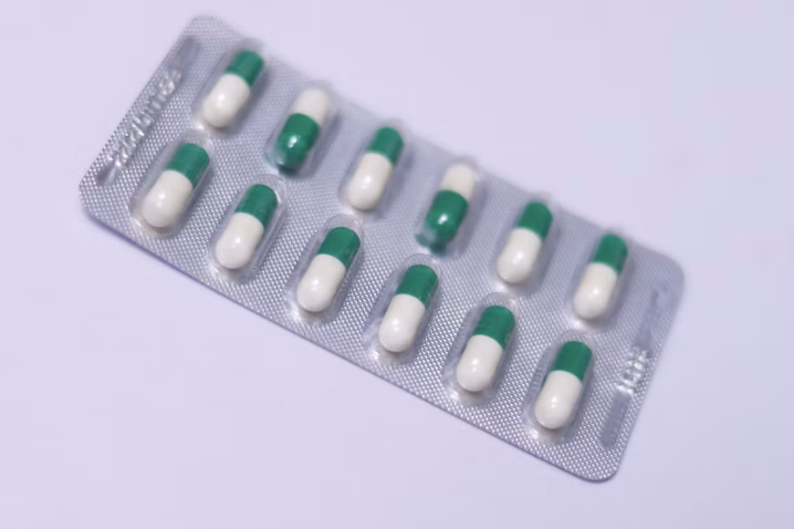 Green-and-white capsules arranged in a silver blister pack on a light purple surface.