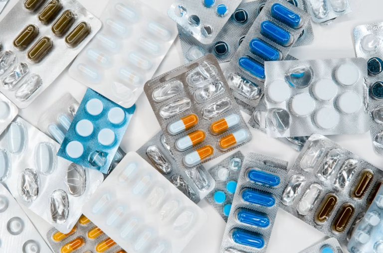 Multiple blister packs containing blue, white, orange, and brown tablets and capsules arranged across a white surface.