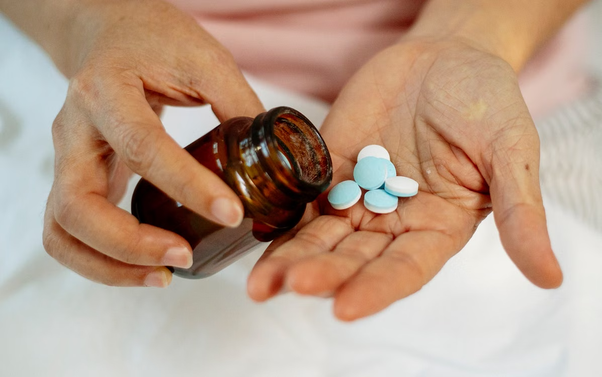Person pouring several blue and white tablets from a brown prescription bottle into an open hand.