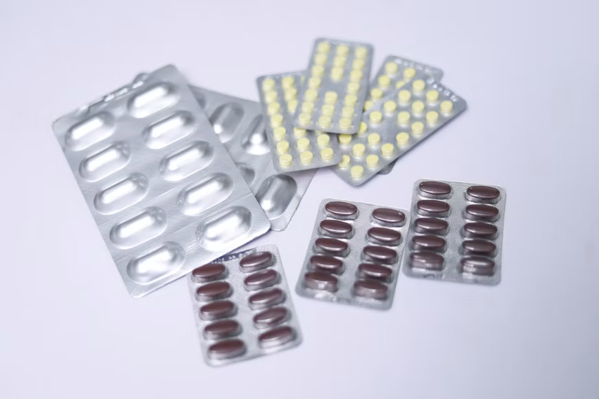 Several silver blister packs containing white, yellow, and dark-colored tablets arranged on a light-colored surface.