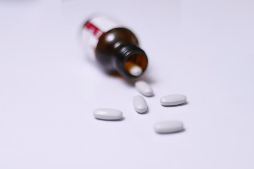 White pill bottle and blister packs containing medication placed on a light-colored table.