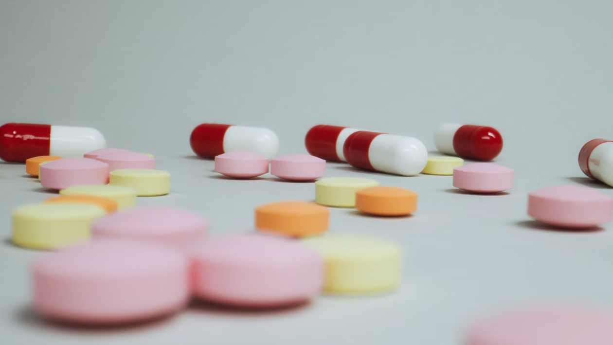 Assorted pink, yellow, orange, and red-and-white tablets and capsules arranged on a light surface.