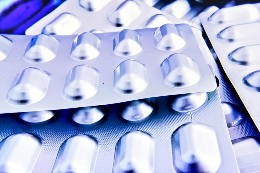 Multiple white tablets in individual blister packs arranged in overlapping layers with blue lighting.
