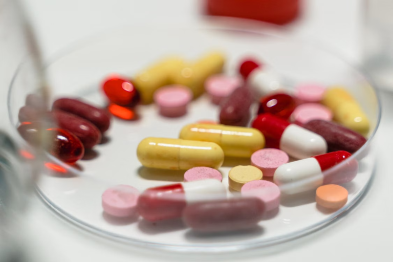 Assorted colorful tablets and capsules arranged on a clear glass dish against a white background.