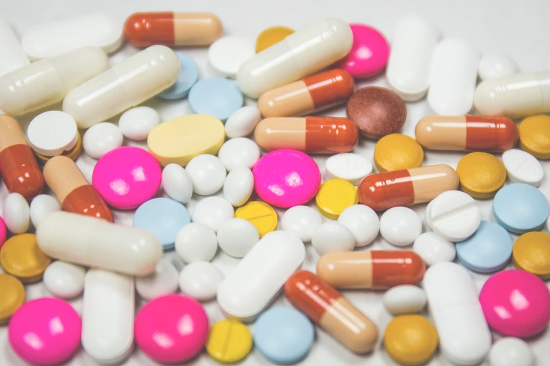 Assorted white, pink, blue, yellow, and orange tablets and capsules arranged across a white surface.