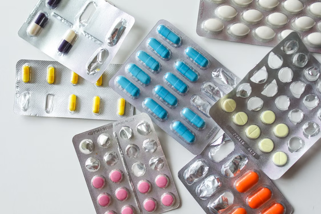 Various pink, white, blue, yellow, and orange tablets arranged in different medication blister packs.